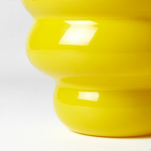 Jarrón de vidrio amarillo brillante, liso y redondeado, sobre fondo blanco. Artesanía de alta calidad visible en el acabado brillante.
