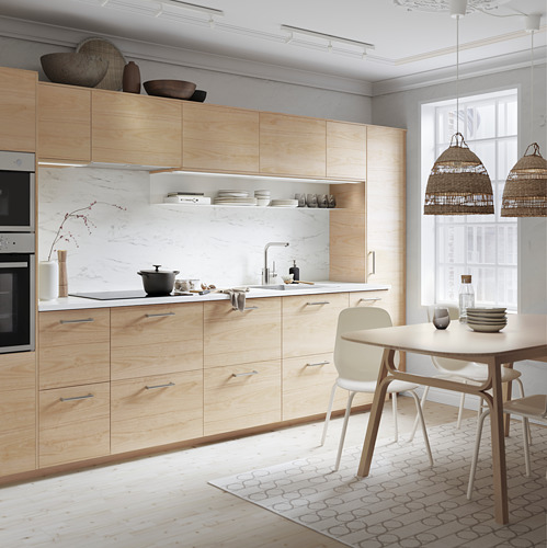 Cocina moderna con gabinetes de madera clara, placa para salpicaduras de mármol, luces colgantes, mesa de comedor y sillas.
