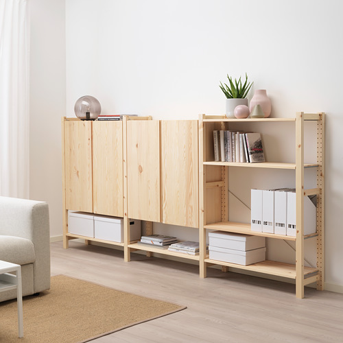 Mueble de almacenaje IVAR de madera ligera, con estantes y armario. Sostiene varios artículos, colocados cerca de un sofá beige en una habitación luminosa.