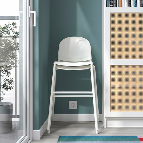 Una silla junior blanca colocada entre paredes verdes, ideal para los niños, que se coloca entre tronas y sillas normales.