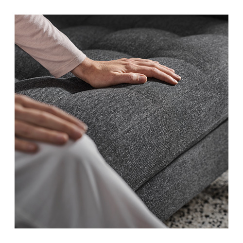 Persona probando cojines de sofá gris, moderno. Las manos presionan el asiento, experimentando la comodidad. Se ven cojines rectangulares grises, afelpados.