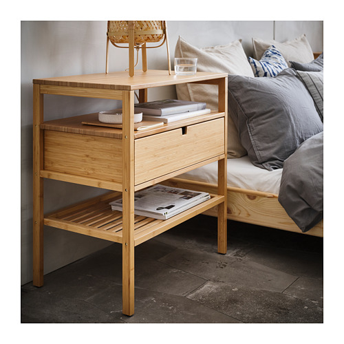Una mesita de noche de bambú NORDKISA con cajón y estantes abiertos. Tiene capacidad para libros, un vaso y tiene un diseño elegante y natural.
