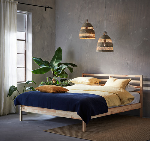 Dormitorio moderno con cama de madera, ropa de cama azul y amarilla, lámparas colgantes, plantas, cortinas transparentes.