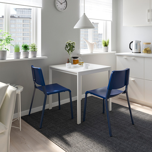 Acogedora zona de comedor con 2 sillas TEODORES azules, mesa blanca a juego, junto a la ventana con plantas y un reloj.