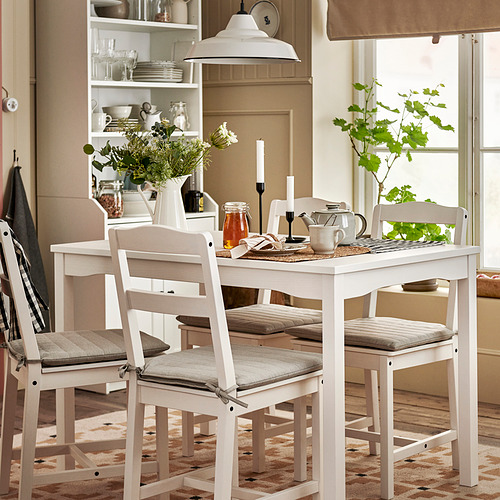 Juego de comedor HAUGA de 4 plazas blanco y brillante con sillas y cojines de madera, perfectamente ajustado debajo de la mesa, flanqueado por estantes abiertos y alfombra.