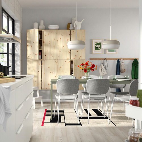 Cocina moderna con gabinetes de pino, sillas blancas y una alfombra vibrante.