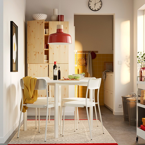 Cocina moderna con mesa blanca, luz roja, estanterías de madera, cuencos, vino, manta amarilla, alfombra, puerta.