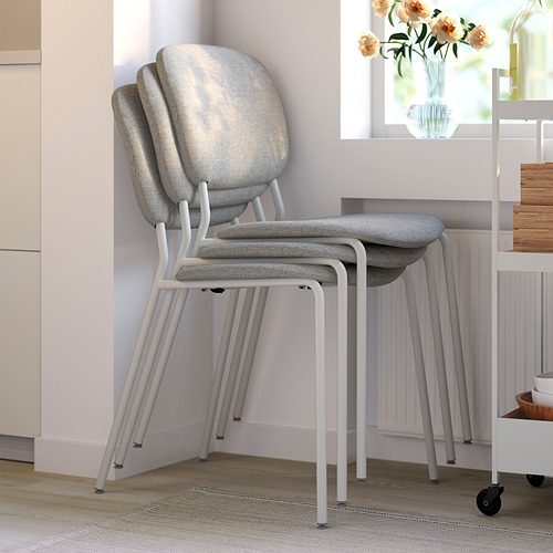 Sillas tapizadas apilables, ideales para comedor u oficina, junto a radiador y flores.