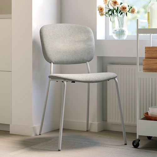 Silla minimalista VIHALS gris claro con asiento acolchado, cerca del radiador y flores.