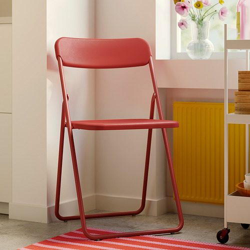 La silla plegable VIHALS de color rojo brillante con asiento y respaldo de plástico, diseñada para un almacenamiento compacto, se mantiene firme contra la colorida decoración de la habitación.