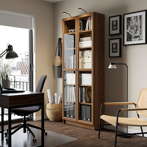 Moderna oficina con librería BILLY, puertas de vidrio, silla de mimbre, escritorio de vidrio y pared de fotos.