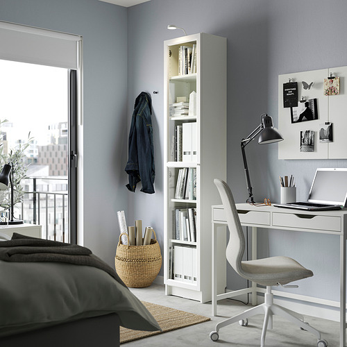 Un dormitorio moderno con estantería blanca BILLY que muestra los medios de comunicación, rodeado de un escritorio y una cama ordenados.