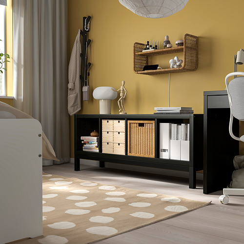Dormitorio moderno con estantería negra KALLAX, cestas, pared amarilla, estantería de mimbre, cama blanca, cortinas grises.