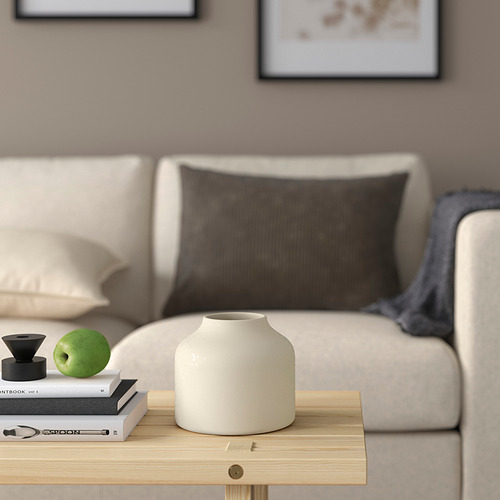 Acogedora sala de estar con sofá crema, almohada, mesa de centro de madera, jarrón BLODBJÖRK, libros, manzana, artículo decorativo y manta.