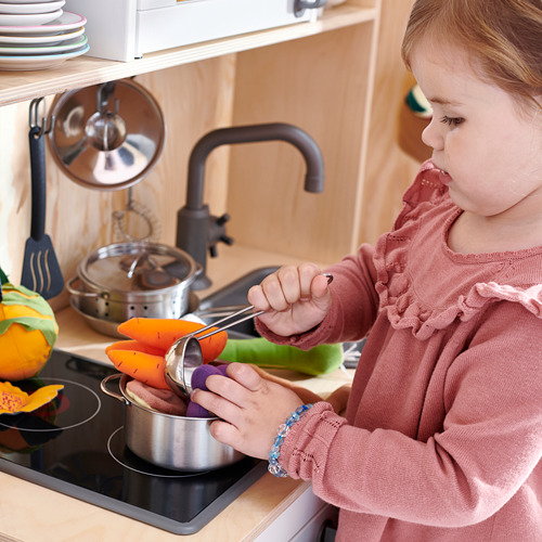 Niño con vestido rosa juega con un juego de cocina de juguete.
