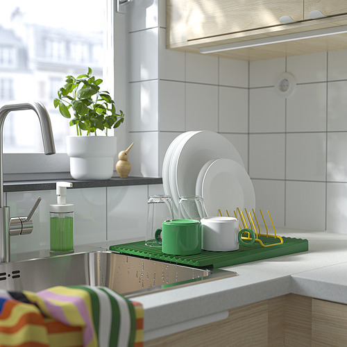 Fregadero de cocina con escurridor de platos verde que sostiene platos, tazas y cubiertos. Al lado está el dispensador de jabón y la planta.