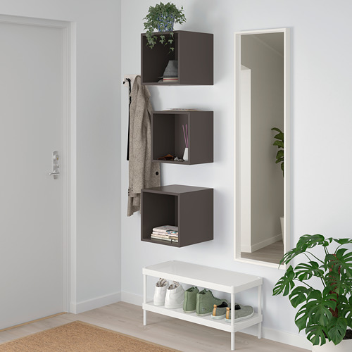 Cubos EKET gris oscuro con planta, libros, cajón; Banco blanco con zapatero, espejo, perchero, chaqueta y planta verde.