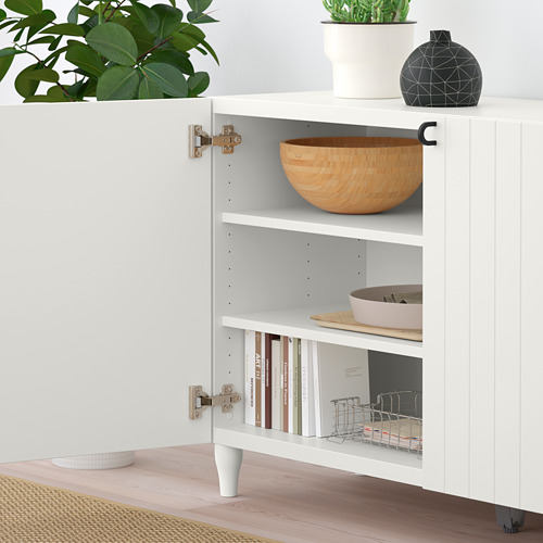 White BESTÅ cabinet with adjustable shelves and integrated soft-close hinges, storing items like bowls, dishes, and books.
