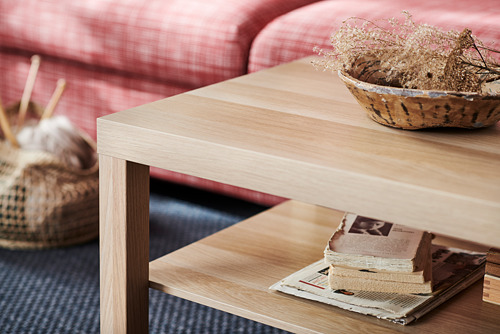 Mesita de madera con relleno de papel alveola, marrón claro. Tiene un estante con revistas apiladas y un cuenco con decoración seca en la parte superior.