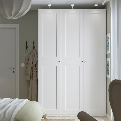 Armario PAX blanco alto y estrecho contra la pared verde salvia, con elegantes pomos y puerta gris cerca. Empequeñece a otros artículos, mostrando una gran capacidad.