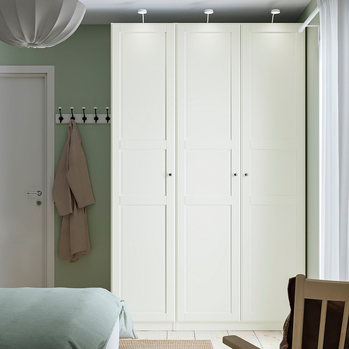 Dormitorio minimalista con armario PAX, paredes de color verde claro. Armario alto, blanco, cabe cerca de la puerta. Barra de colgar a la vista.