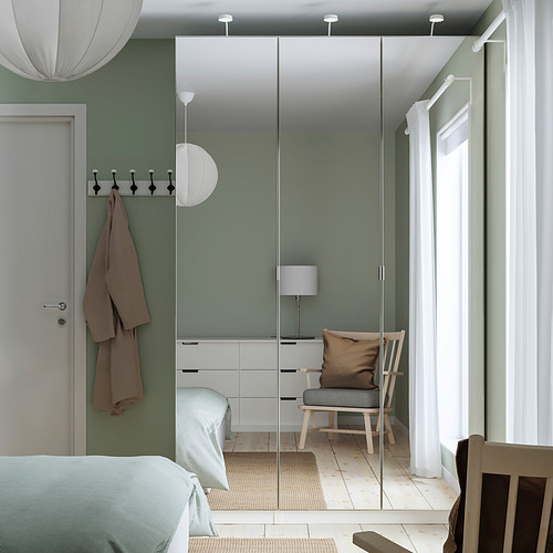 Dormitorio minimalista con paredes verdes, muebles blancos y un gran armario con espejo. Abrigos colgantes, lámpara de noche y decoración tranquila.