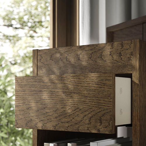 Cajonera de madera oscura de diseño moderno y cajones de cierre suave, colocada cerca de una ventana con vistas verdes al exterior.