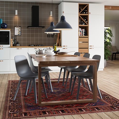 Cocina moderna con mesa de comedor de roble MÖRBYLÅNGA, sillas grises, lámparas colgantes negras, armarios blancos y alfombra roja oscura.
