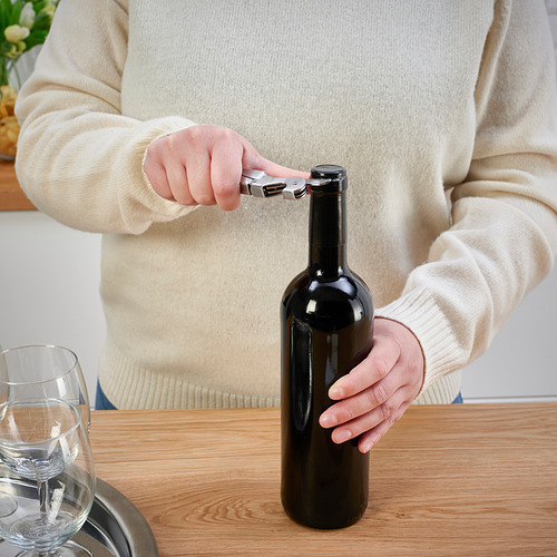 Persona que usa el sacacorchos para abrir la botella de vino en la mesa.