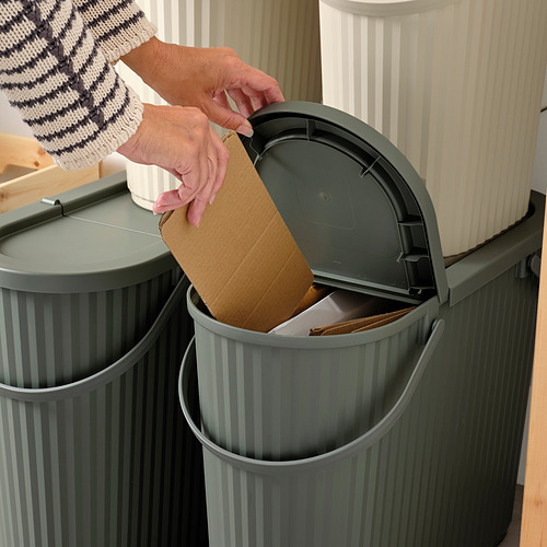 Persona tirando la caja de cartón en el contenedor de reciclaje de DAMMÄNG con la tapa abierta.