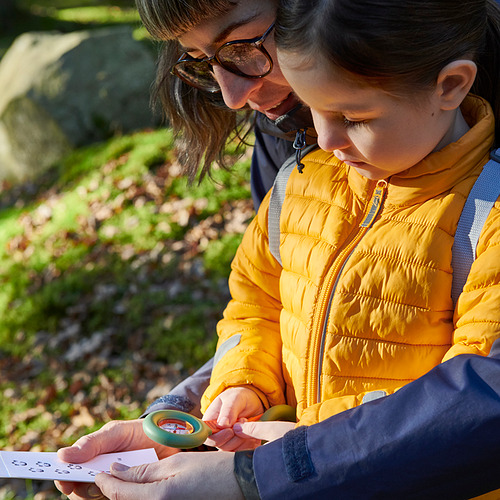 Un niño y un adulto examinan una brújula con una lupa al aire libre.