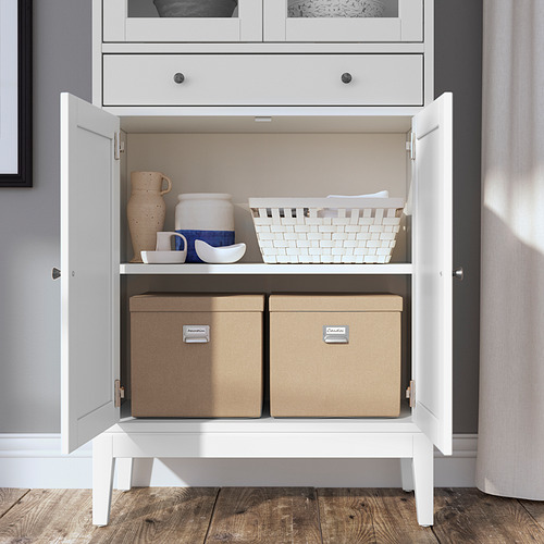 Gabinete blanco con puertas de vidrio, exhibiendo cerámica y cajas de almacenamiento. Diseño moderno y funcional.