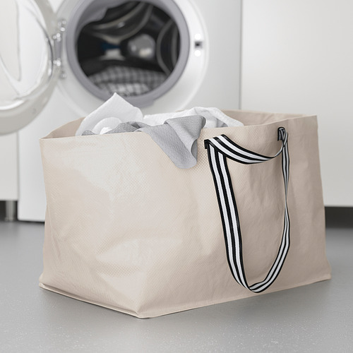 Bolsa de lavandería GÖRSNYGG beige con asas a rayas, en posición vertical junto a la lavadora, llena de ropa ligera.