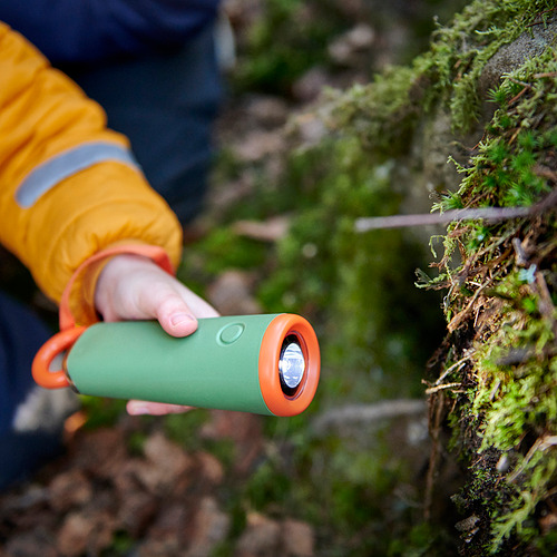 Niño sosteniendo una antorcha LED MAJBAGGE verde y naranja, usando un mecanismo de tracción de cuerda, al aire libre.