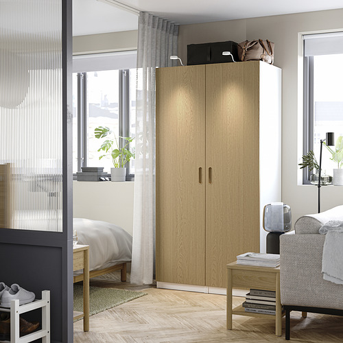A large light wood PAX wardrobe with soft-close hinges next to a bed, illuminated by natural light from a nearby window.