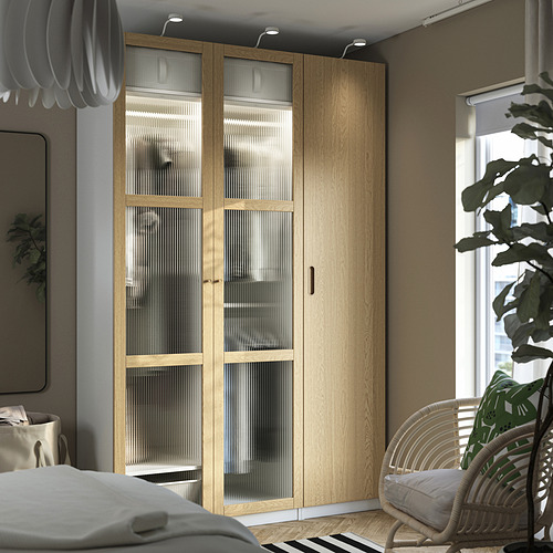 Dormitorio moderno con armario de madera TONSTAD, puertas correderas, silla de mimbre, lámpara colgante, cama y pequeña lámpara de mesa.