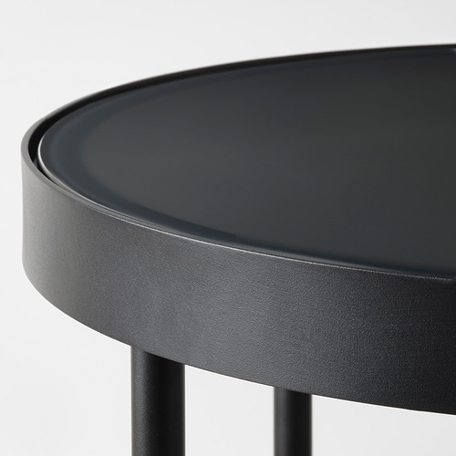 Moderna mesa auxiliar negra con elegante tapa redonda de cristal y robustas patas de metal, que exudan un estilo contemporáneo.