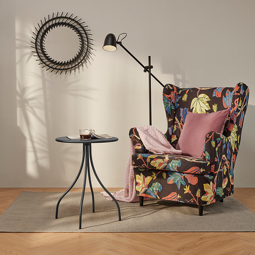 Sillón floral en acogedor rincón con mesa auxiliar, manta, almohada, lámpara, alfombra, decoración.