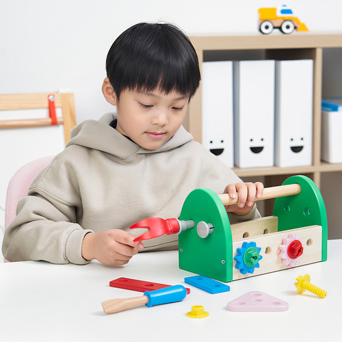 Un niño juega con una caja de herramientas BLOMFLUGA, usando un martillo de plástico rojo para golpear un clavo, desarrollando las habilidades motoras y la creatividad.