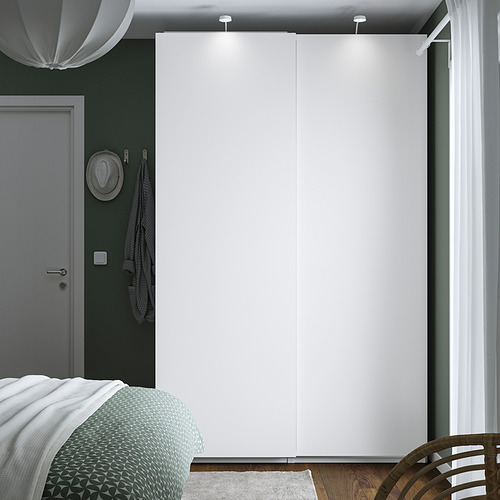 Dormitorio minimalista con gran armario PAX blanco, puerta gris, sombrero colgante y cama con manta verde.