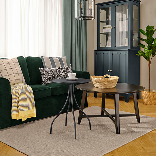 Sala de estar moderna con sofá verde oscuro, mesa auxiliar TÅNEBRO antracita oscura, detalles en negro, alfombra gris claro y planta en maceta.