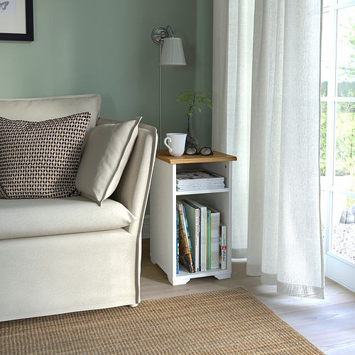 Acogedora sala de estar con mesa auxiliar SKRUVBY junto a un sofá color crema, con libros, taza y planta.
