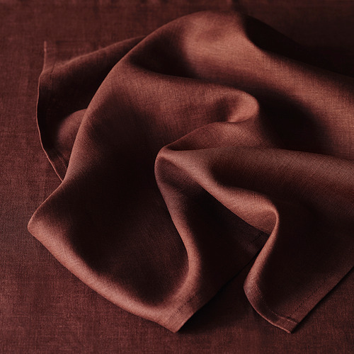 Servilleta de lino marrón oscuro, suavemente arrugada, con una textura natural y un brillo sutil, ideal para mesas elegantes.