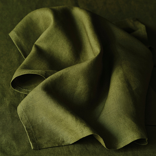 Servilleta de lino verde doblada, que muestra su textura suave y belleza natural, perfecta para elegantes mesas.