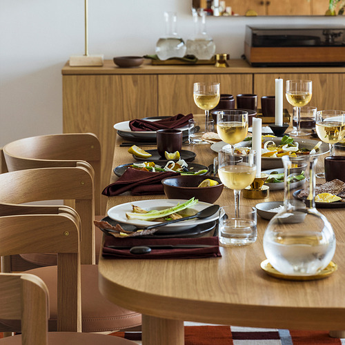 Mesa con platos, cuencos, vasos y velas. Rodeado de sillas de madera y elementos decorativos.