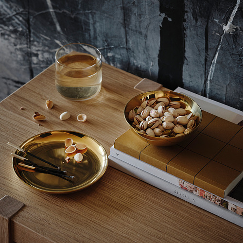 Pequeño cuenco y plato de color latón sobre una mesa con pistachos, fósforos y una bebida. Se utiliza para almacenamiento y decoración.