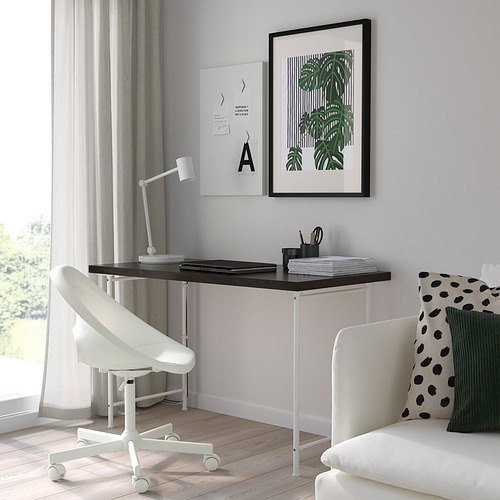 Moderna configuración de escritorio minimalista con escritorio, silla y sofá LAGKAPTEN blancos. La decoración incluye hojas enmarcadas y lámpara blanca.