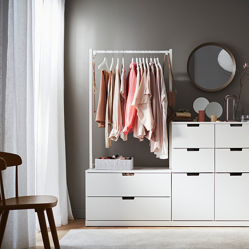 Perchero de madera de la marca BUMERANG en el dormitorio con la ropa, junto a la cómoda y el espejo.