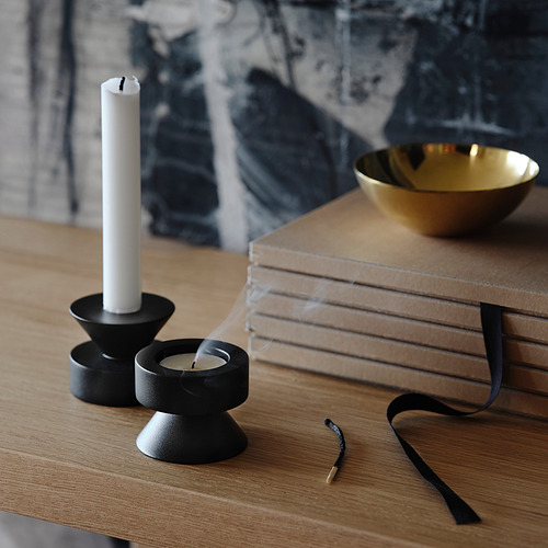 Candelabros de metal negro sobre mesa de madera, uno reversible para candelitas altas y candelitas, cuenco de oro cerca.