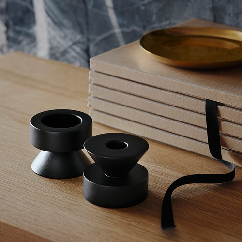 Dos candelabros de metal negro sobre mesa de madera, un lado para velas altas, otro para candelitas, junto a libros apilados y plato de oro.